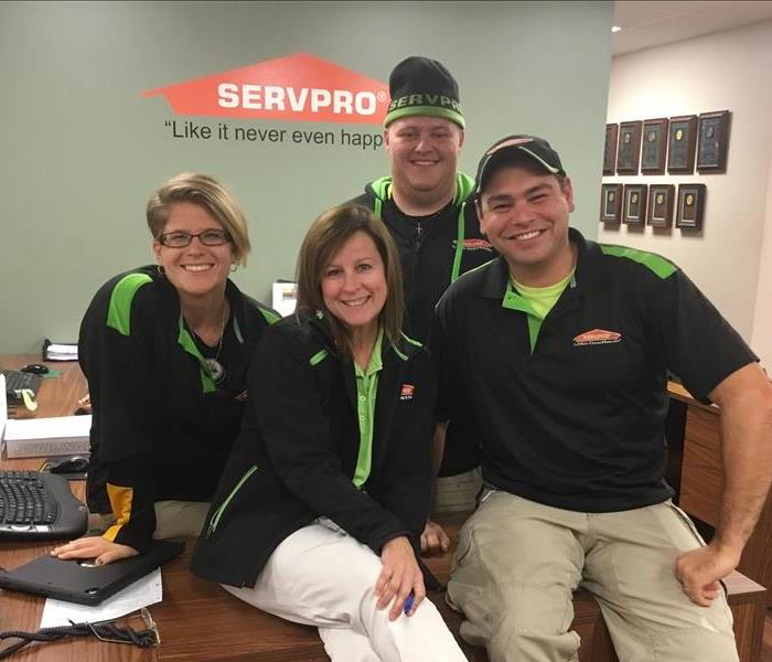 Two males and two females sitting on a desk in a SERVPRO office. 